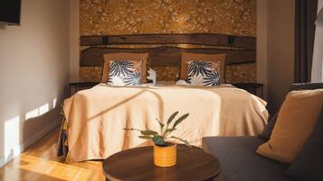 A bedroom with a wooden headboard, floral wallpaper, a bed with beige bedding, and a small round table with a plant.