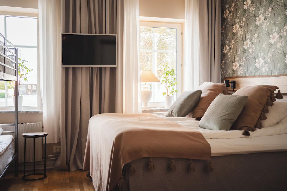 A bedroom with a bed, curtains, a TV, a window, and a plant.