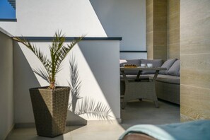 Un espace de détente extérieur moderne, avec un canapé et une table, un pot de fleurs et un mur orné d’un motif géométrique.