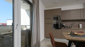 A modern kitchen with a microwave, oven, and coffee maker. There is a dining table with chairs and a sliding glass door leading to a balcony. - Villa Dora - Apartment 4 "Brown" with balcony (Pula)