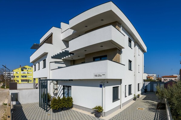 Un immeuble moderne à plusieurs étages, doté d’un toit plat, de grandes fenêtres et d’une entrée sécurisée par un portail.