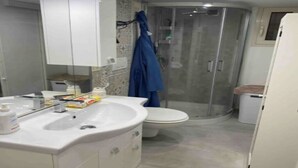 A modern bathroom with a white sink, mirror, and toilet. There is a glass shower enclosure and a white trash bin. - Il loft del vico - Salento (galatone)