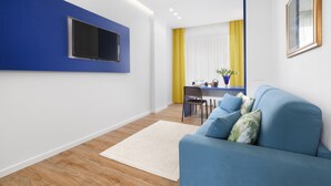 A modern living room with a blue sofa, a flat-screen TV mounted on a blue wall, a wooden floor, and a yellow and white striped curtain. - Shabby Chic sea view apartment (Castellammare di Stabia)