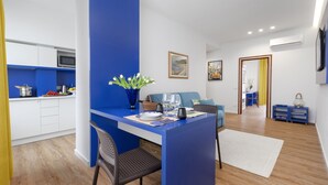 A modern kitchen with white cabinets, a blue accent wall, and a dining area with a blue table and chairs. - Shabby Chic sea view apartment (Castellammare di Stabia)
