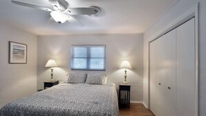 Een slaapkamer met een bed, twee nachtkastjes met lampen, een plafondventilator, een raam met jaloezieën en een garderobe.