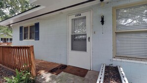 Een wit huis met nummer 1058 op de deur, een houten bankje en een kleine tuin met een bankje en een deurmat.