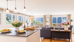 A modern kitchen and living area with large windows, a central island, and a cozy seating area. - Chalet Alpenheim 1 (Lauterbrunnen)