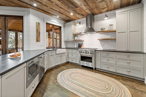 A modern kitchen with white cabinets, a stainless steel range hood, and a wooden ceiling.