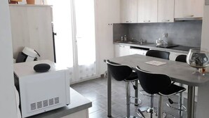 A modern kitchen with white cabinets, a central island with bar stools, and a hanging pendant light. - Air-conditioned house 3 min from Carcassonne, swimming pool (Pennautier)