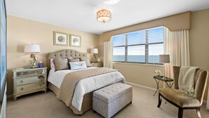 A bedroom with a large bed, bedside tables, a chair, and a window with blinds. - ~ Serenity by the Sea ~ Luxury 2 bedroom Condo, Washer & Dryer! (Myrtle Beach)