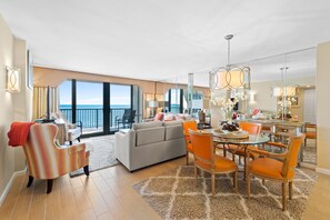 Ein geräumiger Wohnbereich mit großem Sofa, Esstisch und Stühlen, ein Balkon mit Meerblick und modernen Leuchten.