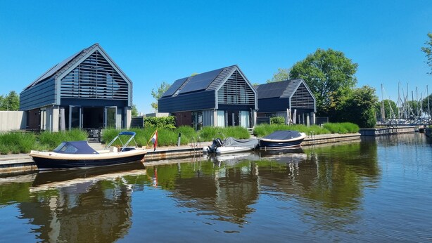 Um canal com três casas modernas e barcos atracados na água.
