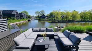 Um terraço com sofá e mesa, com vista para um canal com barcos e casas.