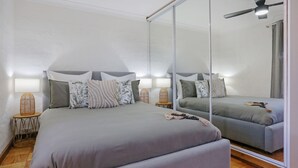 A bedroom with a large bed, two bedside tables, a mirror, and a ceiling fan. - What A View - Lamont St Unit 4 120 (Bermagui)