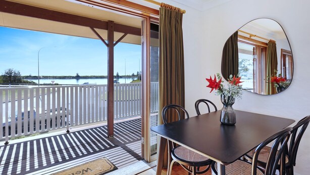 Un balcon donnant sur un lac, une table à manger avec des chaises et un vase rempli de fleurs.