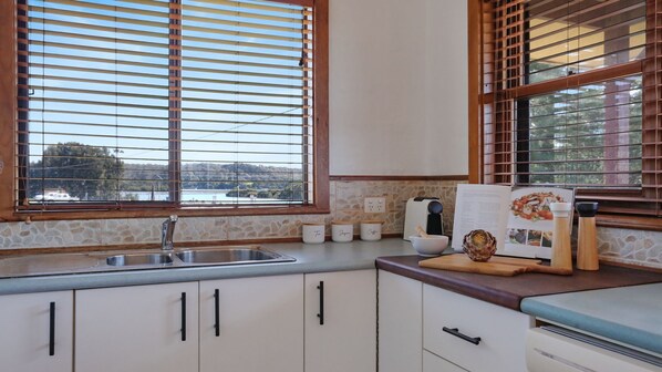 A kitchen with a stone backsplash, wooden cabinets, a sink, and a window with blinds.