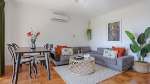 A living room with a sofa, coffee table, dining table, chairs, and a potted plant. - What A View - Lamont St Unit 4 120 (Bermagui)
