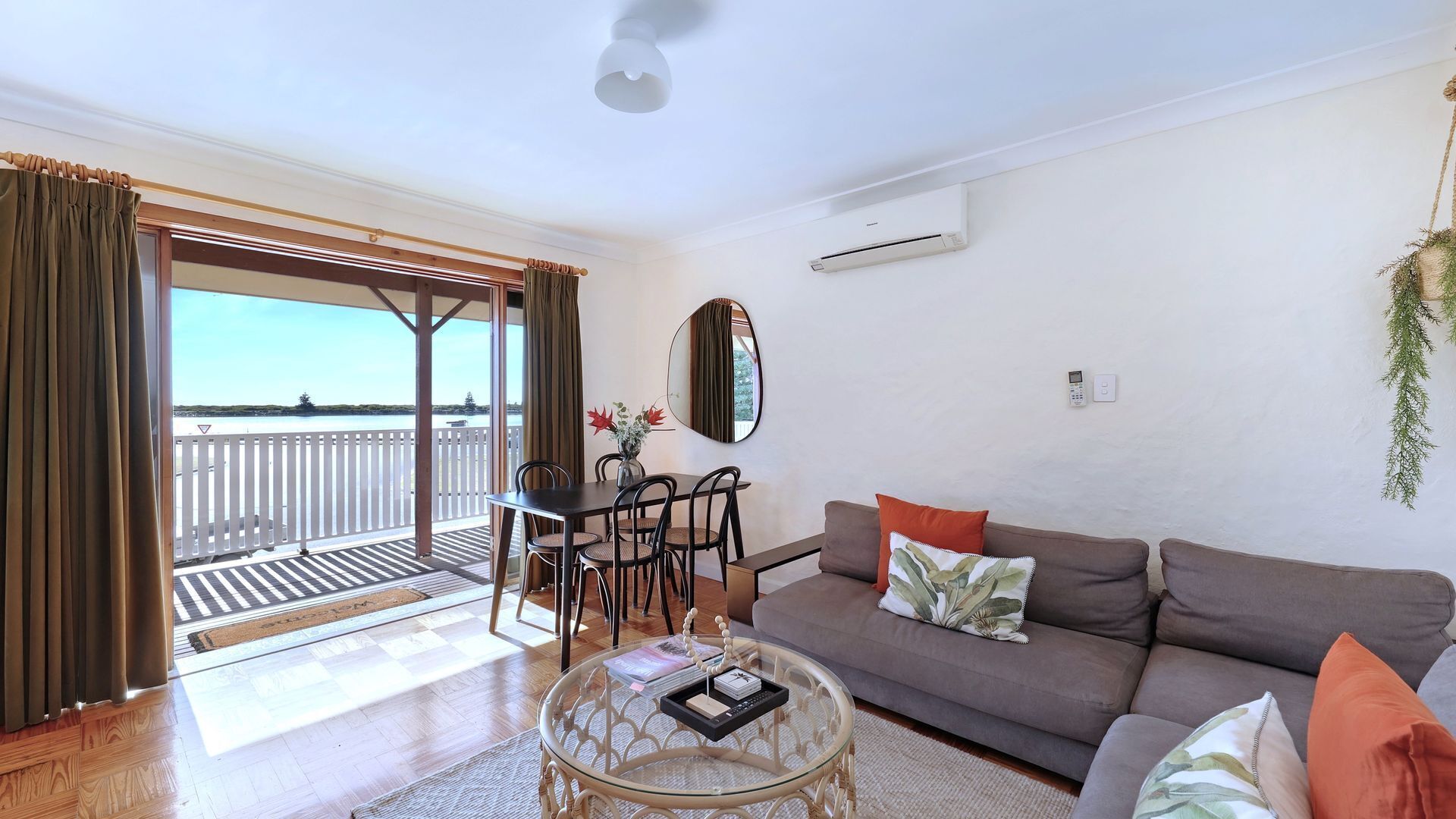 A living room with a sofa, coffee table, and dining area with chairs. There is a view of the sea through large windows.