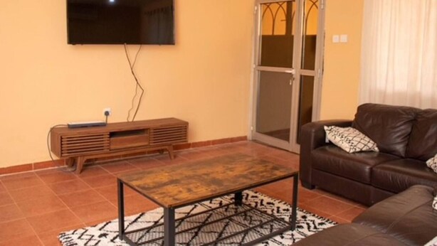 Un salon avec un téléviseur à écran plat fixé au mur, un meuble de rangement en bois, un canapé en cuir marron et un tapis à motifs sur le sol.