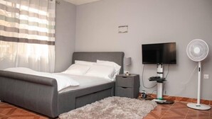 Une chambre à coucher avec un lit, une table de chevet, une télévision et un ventilateur sur pied.