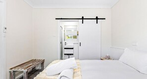 A hotel room with a bed, a bedside table, a bench, a window, and a door leading to a bathroom.