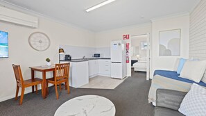 A compact hotel room with a kitchenette, a dining area, a bed, and a small seating area.