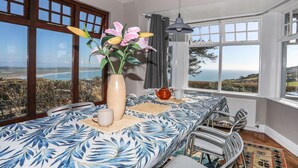 A dining area with a table set for four, a vase with flowers, and a view of the sea. - Bryn Meillion (Pwllheli)