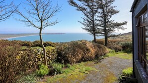 A coastal landscape with a stone wall, a gravel path, and two prominent trees. - Bryn Meillion (Pwllheli)