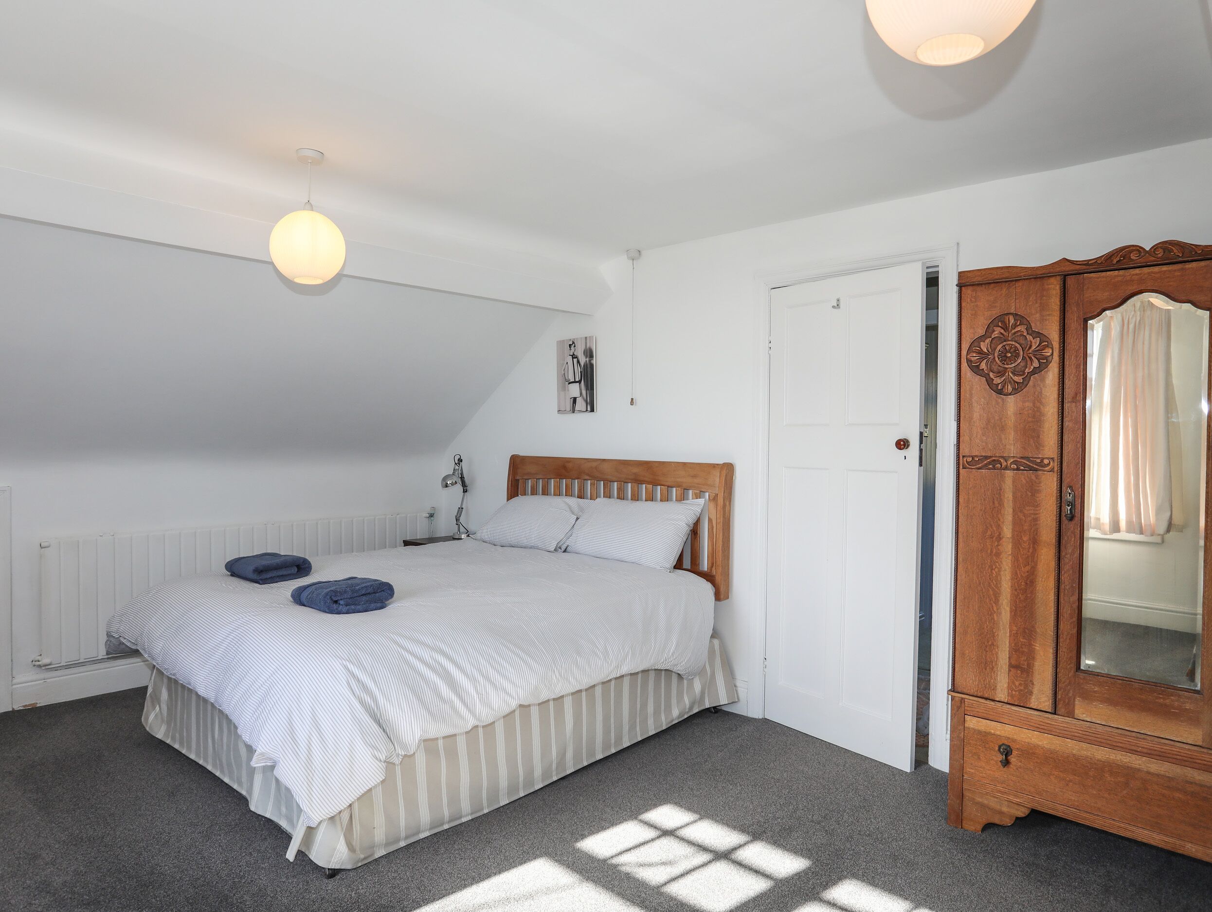 Een slaapkamer met een bed, nachtkastje, houten garderobe en een witte deur.
