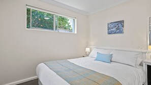 Quarto com cama grande, janela com vista para área verde e quadro na parede.