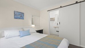 Une chambre d’hôtel comprenant un lit, une table de chevet, un miroir et une porte donnant sur une salle de bain.