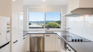 A modern kitchen with a stainless steel dishwasher, a double sink, and a window with a view of a hilly landscape.