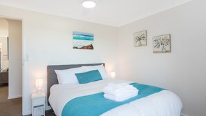 A neatly made bed with a blue blanket and white pillows, a bedside lamp, and a framed painting on the wall.