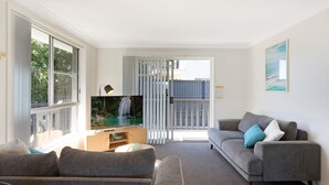 A living room with a TV, grey sofa, and a view of a waterfall through a sliding door.