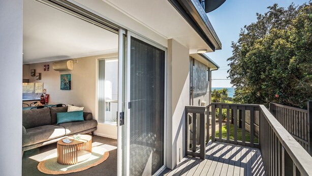 A balcony with a wooden railing, a sofa, a coffee table, and a view of the ocean.