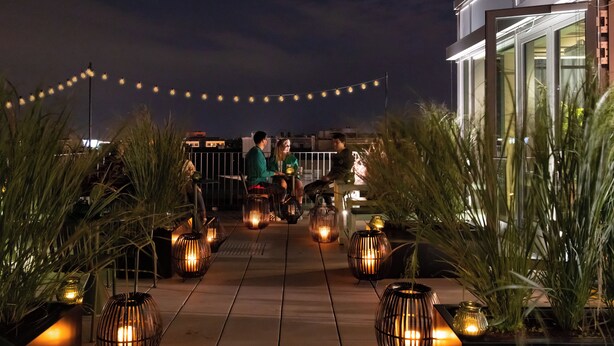 Una terraza en la azotea con luces colgantes, plantas en macetas y faroles.