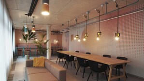 Una sala de reuniones moderna con una larga mesa, sillas negras, un sofá beige e iluminación colgante.