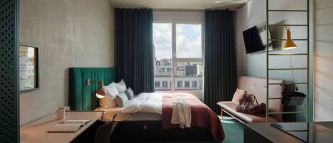 Habitación de hotel con cama, escritorio, silla y televisor fijado a la pared.