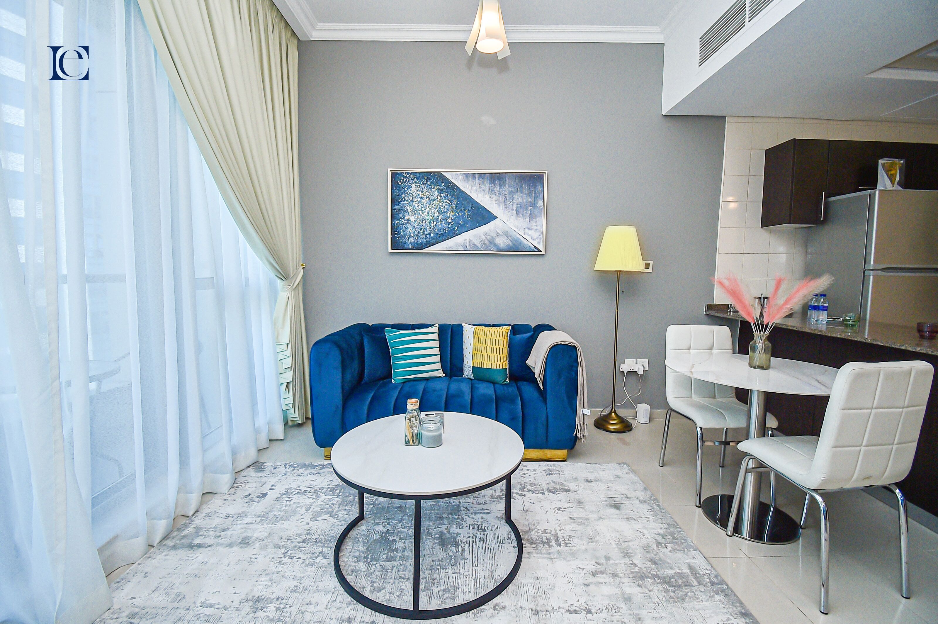 A modern living room with a blue sofa, a round coffee table, and a dining area with white chairs.