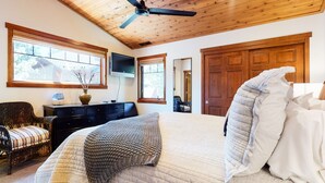A bedroom with a wooden ceiling, a bed with white bedding, a television on the wall, and a window with a view of trees. - Pet-Friendly, 5-Star Home, Private Hot Tub, 2-Car Garage, Walk to The Village (Mammoth Lakes)