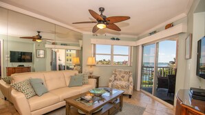 A spacious living room with a beige sofa, a glass coffee table, and a ceiling fan.