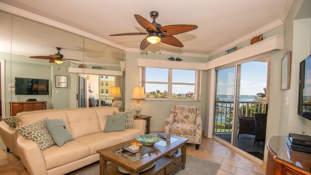 A spacious living room with a beige sofa, a glass coffee table, and a ceiling fan. - Gorgeous Bay Views | Shore Retreat (St. Pete Beach)
