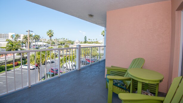 A balcony with a view of a parking lot and buildings, featuring green chairs and a table.