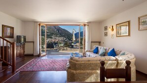 Ein Wohnzimmer mit einer Couch, einem Fernseher und Blick auf eine gebirgige Landschaft durch eine Glastür.