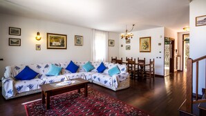 Ein Wohnzimmer mit Sofa, Couchtisch und einem gemusterten Teppich. An den Wänden befinden sich gerahmte Bilder und ein Chandelier.