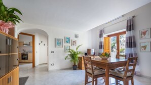 Un vaste espace dédié à la salle à manger, avec une table et des chaises en bois, une plante en pot et une vue sur la ville, visible à travers une fenêtre ornée de rideaux.