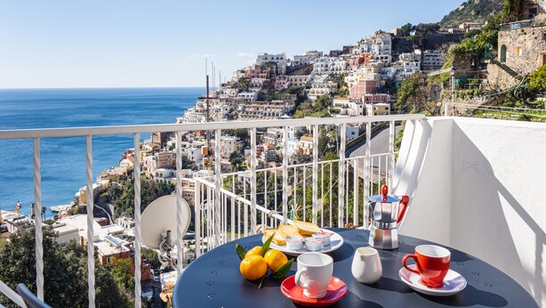 Un balcon avec une table dressée pour le petit-déjeuner, donnant sur une ville côtière.