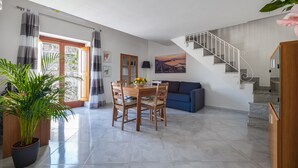 Un vaste espace de vie comprenant une table à manger, des chaises, un canapé, un escalier et une grande plante en pot.