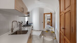 Une cuisine moderne avec des meubles blancs, un évier en acier inoxydable et une cuisinière à gaz. On y trouve également un coin repas avec une table dressée pour deux personnes et une chaise.