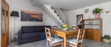 A dining area with a wooden table and chairs, a sofa, a staircase, and a cityscape painting.